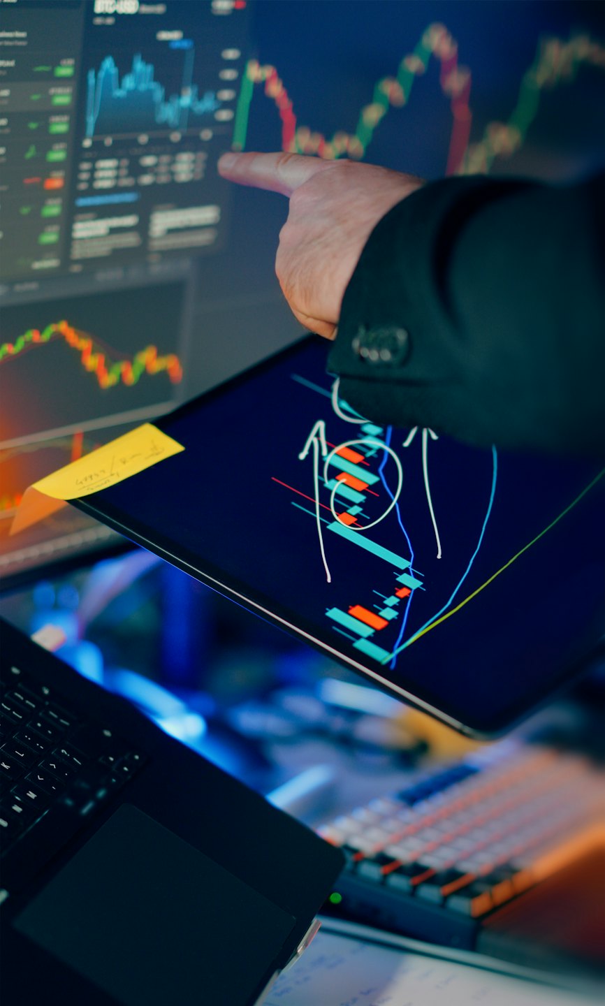 Hand pointing at financial charts on a monitor.