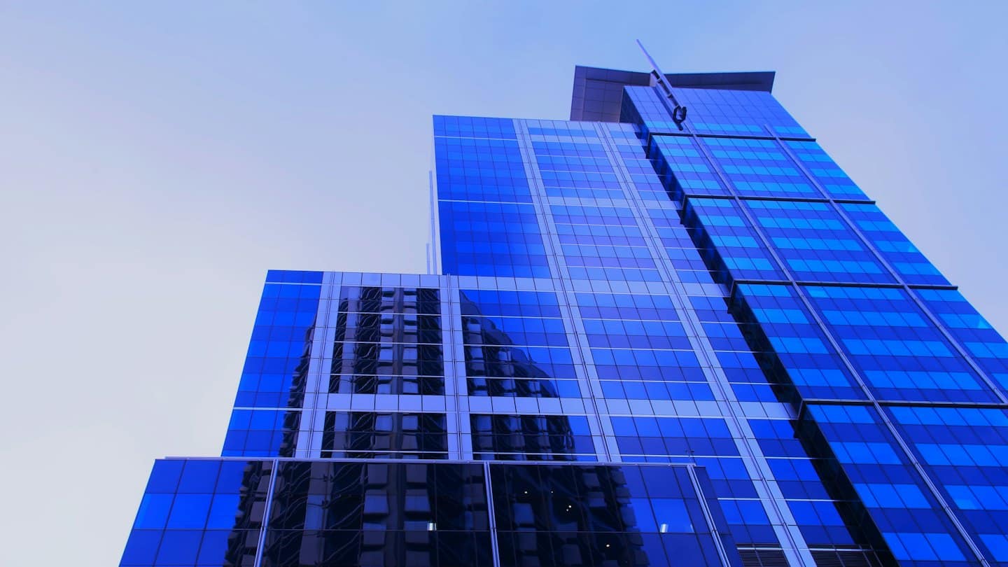 Modern blue glass skyscraper reflecting the surrounding city skyline.